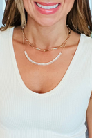 2 gold necklaces on a woman's neck. 2 gold necklaces, one is a chunky paper clip link style, the other one is a delicate chain with baguette cut rhinestones at the center