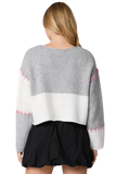 Woman wearing a gray and white colorblock sweater with pink hand stitch detail.  Skirt is paired with a black mini skirt. Photo is taken from the back