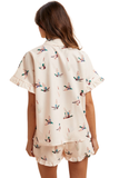Woman modeling a silky satin feel mallard duck print matching set featuring a button down collared top with feminine ruffle sleeves and coordinating relaxed fit ruffle hem shorts.