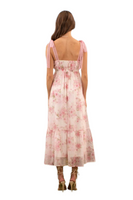 Back view of a woman wearing a pink floral maxi dress with crochet lace tie straps, showcasing delicate details and a flowy, feminine silhouette.