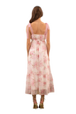 Back view of a woman wearing a pink floral maxi dress with crochet lace tie straps, showcasing delicate details and a flowy, feminine silhouette.