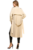 woman wearing a pleated trench coat. Photo is displaying the back of the trench coat. Coat has a waist tie 