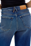 Close-up back view of a person wearing blue denim jeans, showing the waistband, belt loops, back pockets, and a tan leather Cello brand patch.