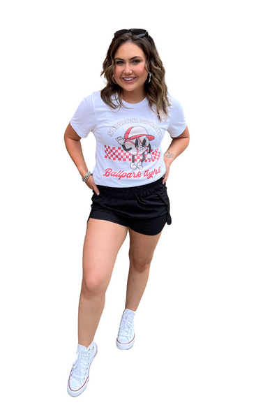 Woman wearing a white graphic tee with black athletic shorts. Graphic tee reads "Summer Nights Ballpark Lights" with a baseball mascot character on front