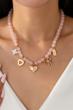 Pink beaded charm necklace worn on model, featuring gold heart, bow, clover, and floral charms for a feminine layered jewelry look