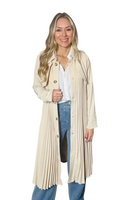 woman wearing a beige pleated trench coat. Coat is called has brown buttons down the front 