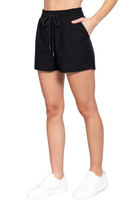 side view of black drawstring linen style shorts, woman's hand is resting in the front pocket 