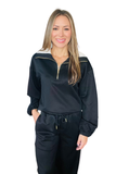 A woman modeling a black satin half-zip sweatshirt and matching sweatpants set with white and gold accents, set against a plain white background.