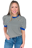 A woman modeling a short-sleeve ringer top with black and white horizontal stripes and bright blue trim on the crew neck, cuffs, and sleeves, paired with blue jeans against a plain white background.