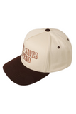 Cream and brown trucker hat with a brown bill, brown squatchee, and matching brown eyelets. The front features embroidered brown text that reads, “JESUS SAVES I SPEND.”