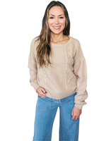 Woman wearing a neutral beige cable knit sweater with long sleeves and a relaxed fit, paired with light blue wide-leg jeans.