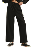 Black wide-leg sweatpants with a drawstring waist and white side stripes, shown on a model from the waist down wearing black sneakers against a white background.