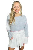 Woman wearing a gray and white colorblock sweater with pink hand stitch detail.  Sweater is styled with a white pleated skirt