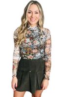 woman wearing a floral long sleeve turtleneck with a olive green corduroy pleated skort 