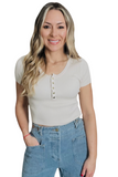 woman wearing a cream ribbed short sleeve top with gold snap buttons on the front center of the shirt. Shirt is paired with wide leg blue jeans 