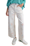 White cropped twill pants with pastel floral cross stitch inspired print, wide leg silhouette, relaxed fit, side pockets, and raw hem detail paired with green sneakers.