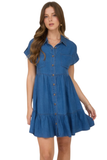 Woman wearing a blue chambray mini dress with a collared button-down front, cuffed short sleeves, chest pockets, and tiered ruffle hem detailing.