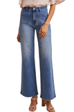 A model wearing a pair of high-waisted, wide-leg blue denim jeans with a faded wash, styled with a light pink blouse and brown heeled sandals against a plain white background.