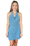 A woman modeling a sleeveless light blue denim halter dress with a button-front closure, photographed against a plain white background.
