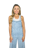 Woman wearing a white tank top with frayed wide leg denim overalls 