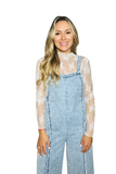 Woman wearing white lace mesh shirt under light denim overalls with frayed detailing 