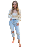 Woman wearing a white sweater and high rise light wash denim jeans with distressing on one knee