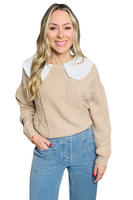 woman wearing a tan cable knit sweater with a white doll collar, sweater is paired with light blue denim 