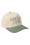 Cream and sage green trucker hat with a sage bill, sage squatchee, and matching sage eyelets. The front features embroidered teal text that reads, “JESUS SAVES I SPEND.”