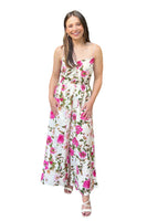 Woman wearing a spaghetti strap floral print jumpsuit. Jumpsuit is ivory with light and bright pink florals