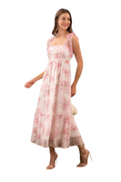 Woman wearing a white and pink floral maxi dress with a square neck line. Dress is an empire waist with crochet detailing along the top and straps. 