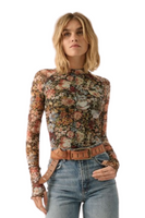 Woman wearing a flor semi-sheer long sleeve floral print shirt. The shirt has exposed seams, a ,mock neckline and ruffle detailing on the sleeves. Woman is wearing blue jeans and a light camel belt with the floral top 