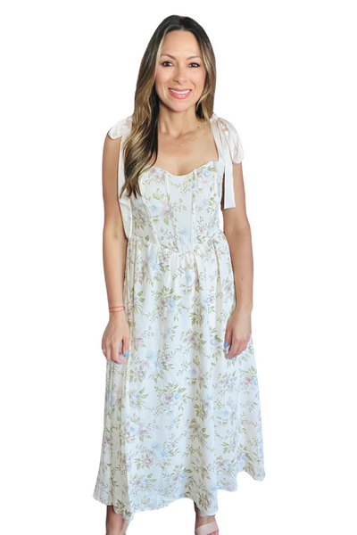 Woman wearing a maxi dress with a floral print. Dress has a corset style top with satin tie straps