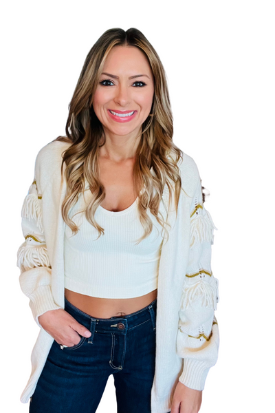 Woman wearing a cream shirt and jeans with a cream zip up cardigan with fringe detailing on the sleeve