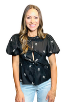 Woman wearing a black top with a round neckline, short puffy sleeves, 3 front tie bow closure, and white bow embroidery