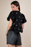 Woman wearing a black top with a round neckline, short puffy sleeves, 3 front tie bow closure, and white bow embroidery