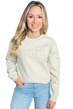 Woman wearing a tan unisex sweatshirt with 4 embroidered gingerbread man cookie across the front center. Woman is wearing it with light denim jeans