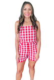 Woman wearing a red and white gingham romper with adjustable straps, scallop trim detailing at the waist and shorts, and a fitted summer silhouette.