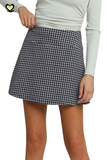 A model wearing a black and white gingham mini skirt with a front welt pocket, paired with a light sage green long-sleeve top, shown against a plain white background.