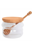 A clear glass honey jar with a light natural wood lid and matching wooden honey dipper, shown on a plain white background.