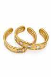 Three gold cuff bracelets with beaded edges and rectangular clear stones, arranged on a plain white background.