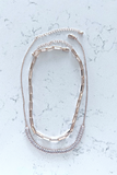 Gold necklace set on a white marble background. 2 gold necklaces, one is a chunky paper clip link style, the other one is a delicate chain with baguette cut rhinestones at the center