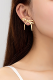 gold herringbone chain bow stud earrings on a woman's ear. 