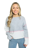 Woman wearing a gray and white colorblock sweater with pink hand stitch detail. 