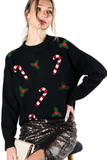 Woman wearing a black Christmas sweater with red and white candy cane patches and green holly appliqués, styled with a sequined skirt.