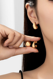 puffy huggie style earrings being held up to an ear for sizing reference 