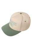 Cream and sage green trucker hat with a sage bill, sage squatchee, and matching sage eyelets. The front features embroidered teal text that reads, “JESUS SAVES I SPEND.”