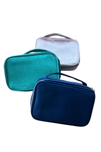 three jewel tone rectangular cosmetic bags with handle. Bags are blush, emerald green and blue 