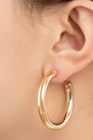 A pair of large gold hollow tube puffy hoop earrings with a polished finish, measuring 1.75 inches in diameter on a woman's ear.