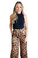 Woman wearing a black mock neck tank top tucked into a pair of leopard drawstring straight leg pants