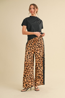 woman wearing a black short sleeve mock neck shirt with a pair of straight leg leopard pants with a black stripe down the side.